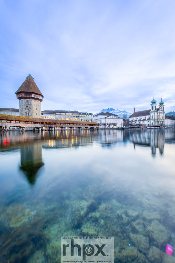 Kapellbrücke und Wasserturm Luzern bei Dämmerung | Spiegelung. Stein. Stille.Die sanfte Spiegelung des historischen Wasserturms im ruhigen Flussbett der Reuss erzeugt eine fast magische Symmetrie. Das warme Licht der Brücke bildet zur blauen Stunde einen fesselnden Kontrast zum kühlen Stein dieses Wahrzeichens.Wähle unter "Produktauswahl" dein Wunschformat: Vom klassischen Wandbild über Puzzle &amp; Tassen bis zum digitalen Download (z.B. als Handy-Hintergrund). - Realisiert mit Pictrs.com