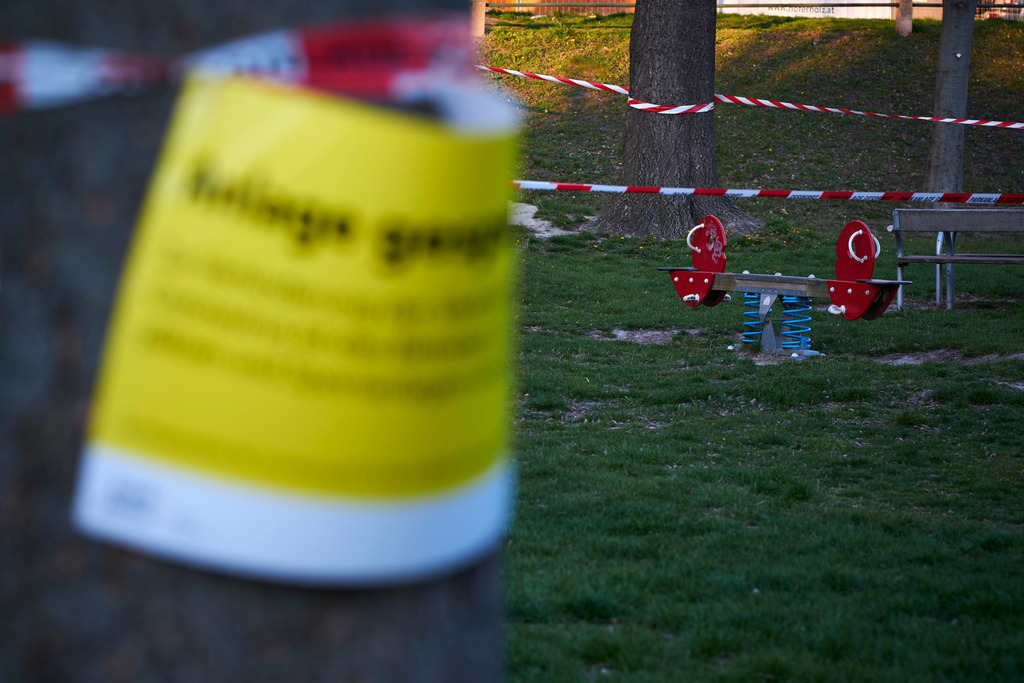 Absperrband vor einem Spielplatz | Wien, Austria - April 01, 2020: Massnahmen zur Einschränkung von COVID-19; Absperrband vor einem Spielplatz, im Vordergrund eine gelbe Hinweistafel. - Realisiert mit Pictrs.com