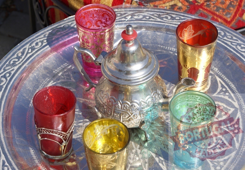 Moroccan mint tea set serving hospitality and tradition | Moroccan tea set with silver teapot and colorful traditional glasses on an ornate metal tray - Realisiert mit Pictrs.com