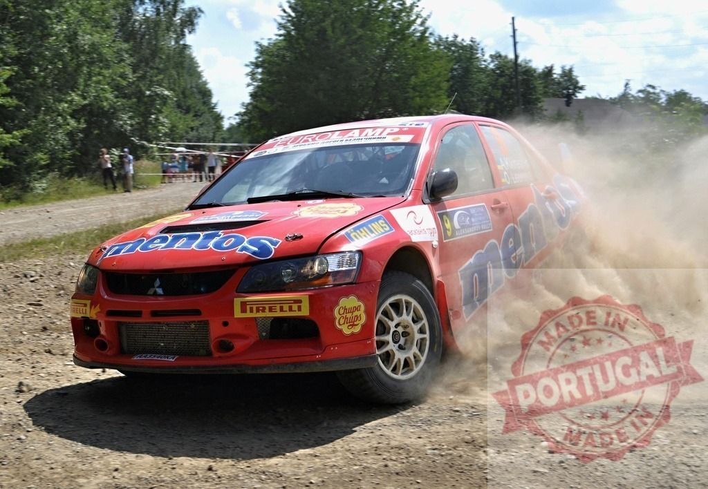 Mitsubishi Lancer Evolution rally car kicking up dust | Red Mitsubishi Lancer Evolution rally car speeding on a dirt road during competition - Realized with Pictrs.com