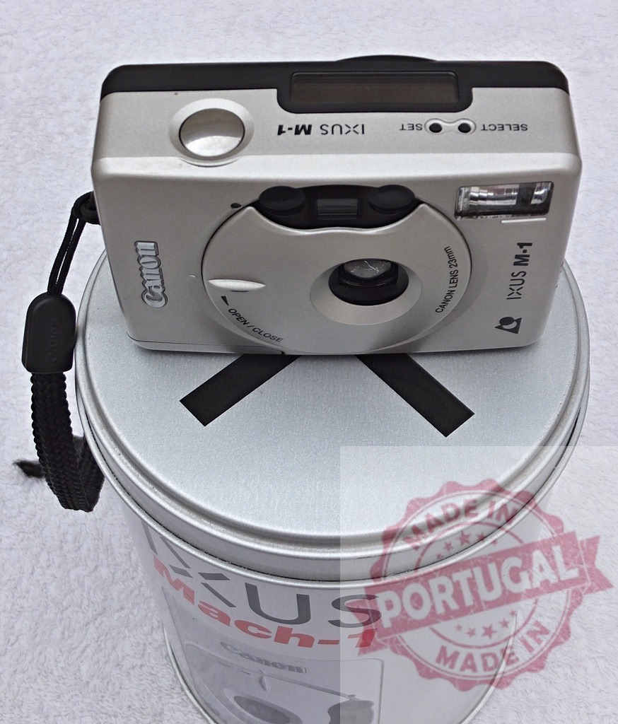 Canon IXUS M-1 camera on silver tin box | Canon IXUS M-1 compact APS film camera showcasing vintage photography technology - Realized with Pictrs.com