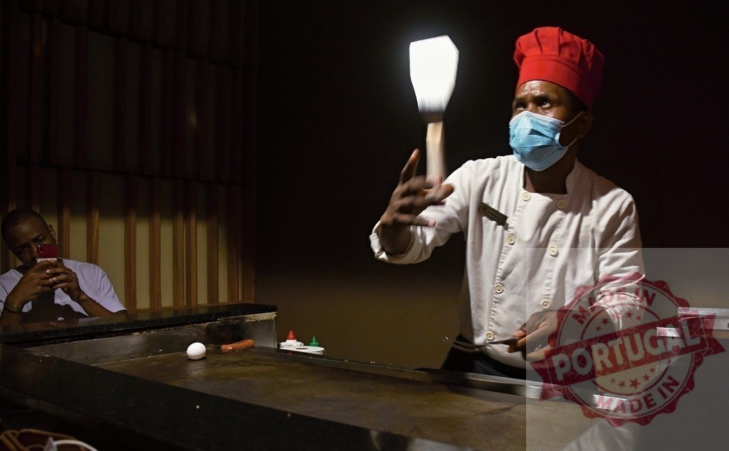 Black chef performing teppanyaki cooking skills wearing mask | Black chef juggling spatulas during a teppanyaki cooking performance in a restaurant - Realisiert mit Pictrs.com