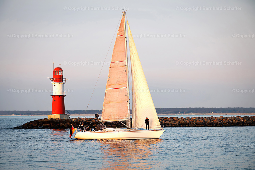 Segler am leuchtturm | Ein Segelboot läuft vor einem roten Leuchtturm an der Ostseeküste in den Hafen ein. - Realisiert mit Pictrs.com