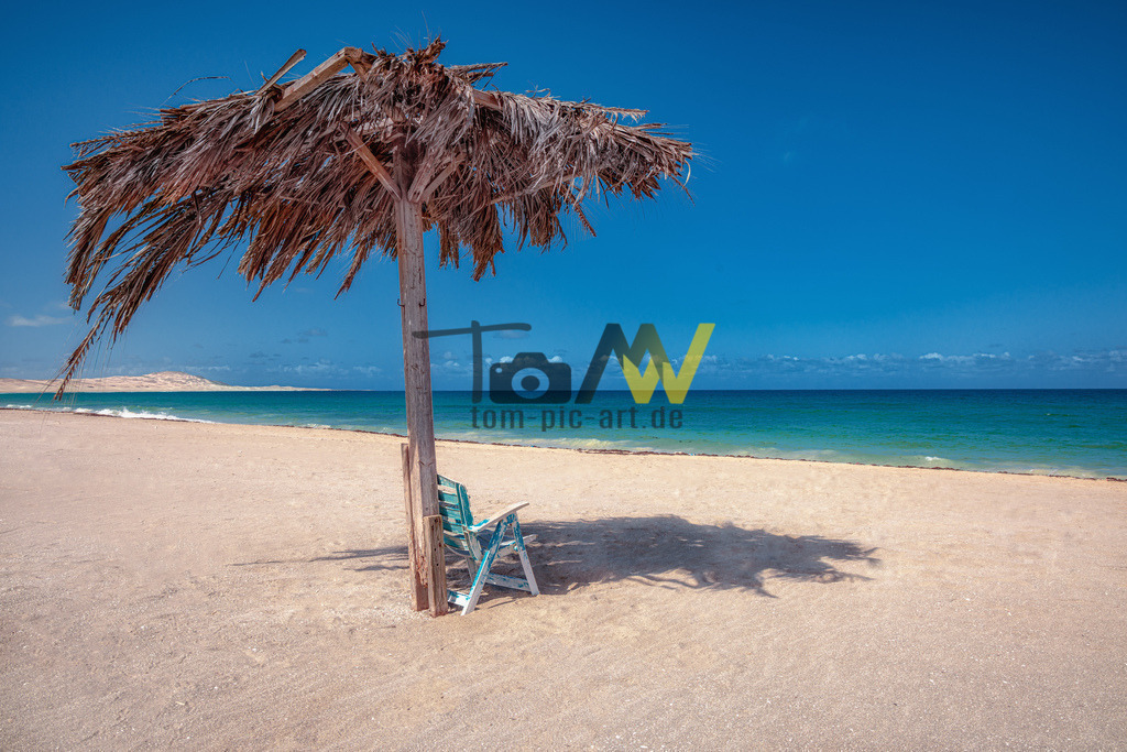 Strandszene auf Boa Vista----Sonnenschirm am leeren Strand | Weiter endloser Strand. Ein Sonnenschirm, tiefblaues Meer, azurblauer Himmel , unter dem Schirm ein kleiner Gartenstuhl. - Realisiert mit Pictrs.com