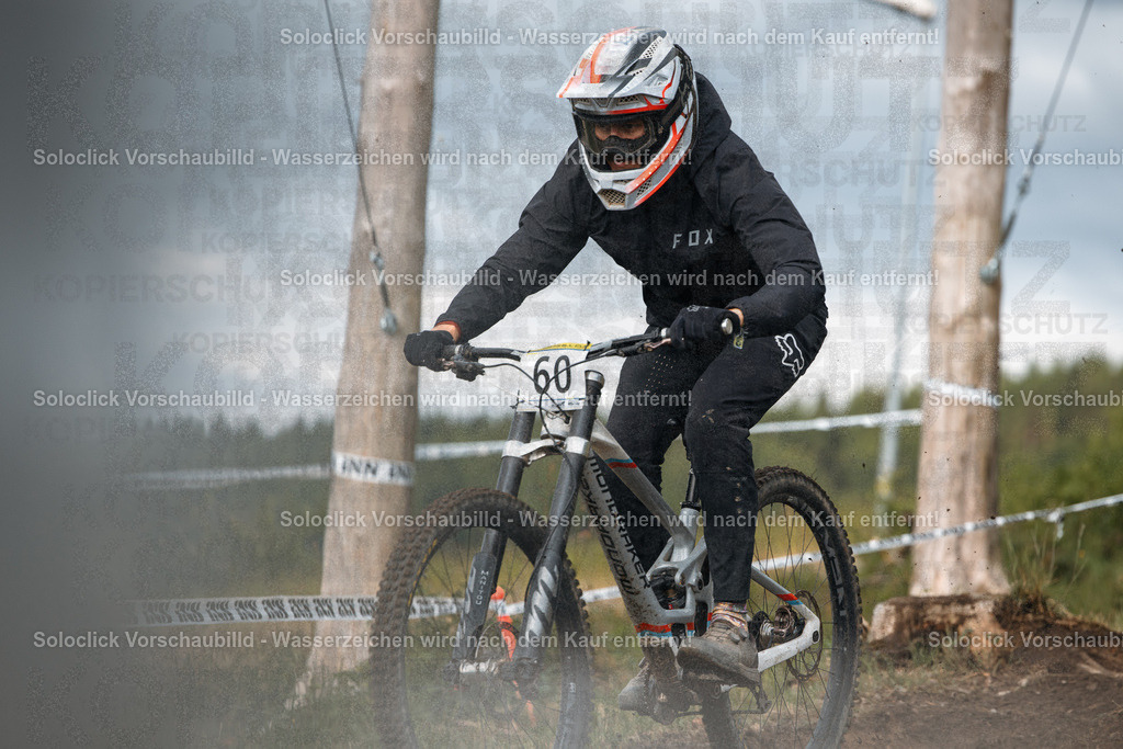 Action im Bikepark Winterberg | Das Foto zeigt einen Mountainbiker während des iXS Downhill Cups 2025 im Bikepark Winterberg, speziell auf der Strecke 'The Mother'. Der Fahrer ist in voller Montur unterwegs und bewältigt eine schnelle Abfahrt. Der Hintergrund zeigt eine staubige Strecke mit Bäumen und einer Absperrung. - Realisiert mit Pictrs.com