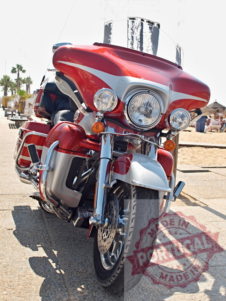 Harley-Davidson touring motorcycle parked by beach | Red and silver Harley-Davidson touring motorcycle parked on pavement with beach background - Realisiert mit Pictrs.com