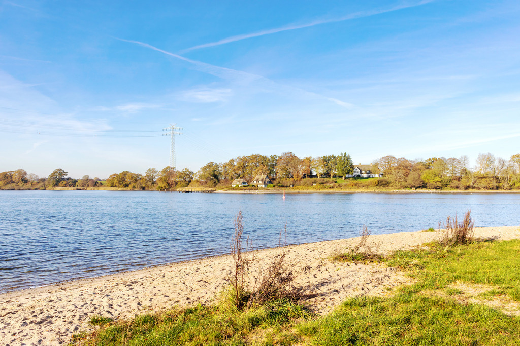 Wandbild: Herbst an der Schlei in Kappeln | Dieses Wandbild im Querformat zeigt die herbstliche Schlei in Kappeln. Im Vordergrund ist der Schleistrand in Ellenberg zu sehen. Der blaue Himmel ist fast wolkenlos. - Realisiert mit Pictrs.com
