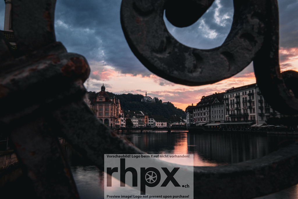 Blick durch das Geländer auf die Luzerner Altstadt / View through the Railing toward Lucerne’s Old Town | Ein besonderer Blick auf Luzern – durch das schmiedeeiserne Geländer eröffnet sich die Sicht auf die Altstadt und die Reuss im warmen Licht der Abenddämmerung.  *************** A unique view of Lucerne — through the wrought-iron railing, the old town and the Reuss River appear bathed in the warm light of evening dusk. A composition that blends architecture, atmosphere, and perspective. - Realisiert mit Pictrs.com