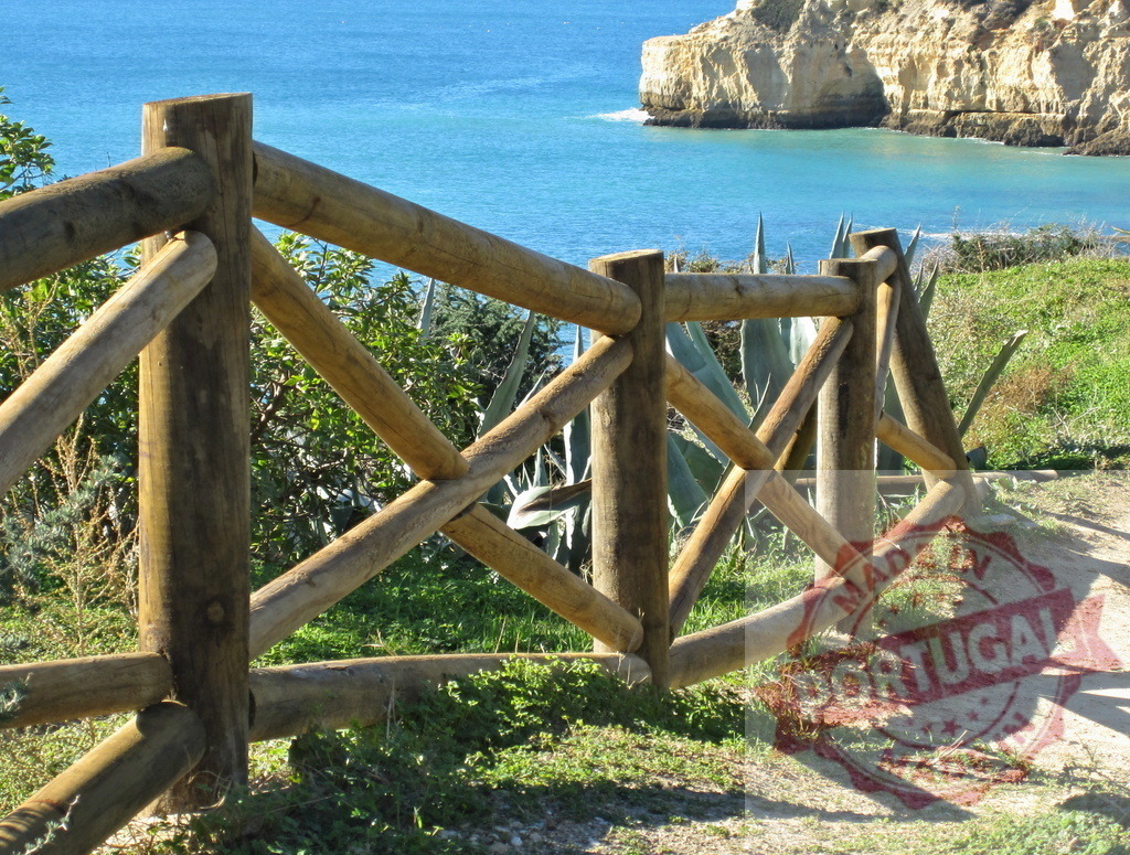 Wooden fence overlooking ocean cliffs and coastline trail. Algarve - Silves | Wooden fence protecting a coastal path along the ocean with cliffs and green vegetation - Realized with Pictrs.com