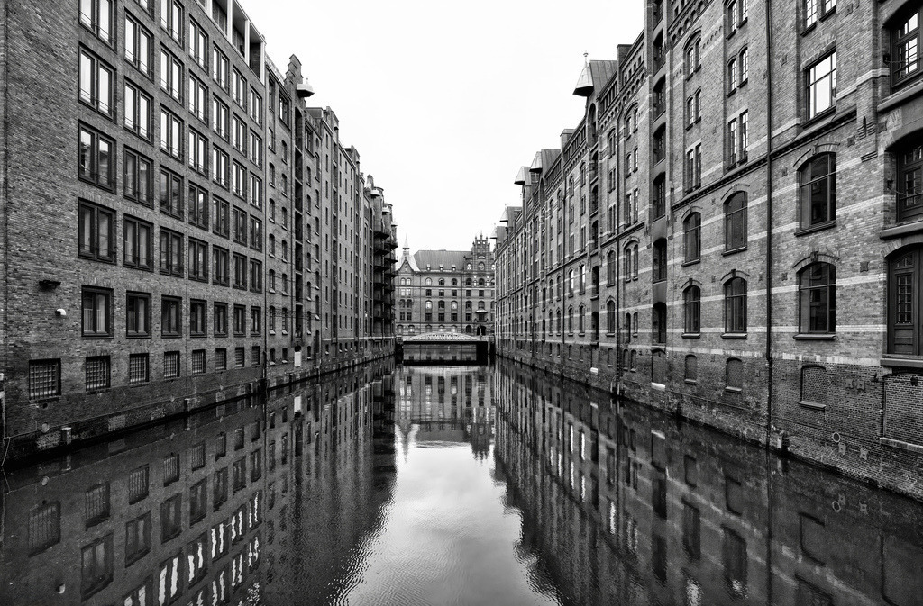 Die Speicherstadt in Hamburg, in schwarz weiß,Altstadt | Das Bild zeigt die Hamburger Speicherstadt. Es handelt sich um den größten zusammenhängenden historischen Lagerhauskomplex der Welt, der zum UNESCO-Weltkulturerbe gehört. Die Speicherstadt wurde zwischen 1885 und 1927 erbaut. Sie liegt südlich der Hamburger Altstadt, zwischen dem Oberhafen und dem Sandtorkai. Die charakteristische Architektur aus roten Backsteingebäuden und Fleeten (Kanälen) spiegelt sich im Wasser wider. - Realisiert mit Pictrs.com