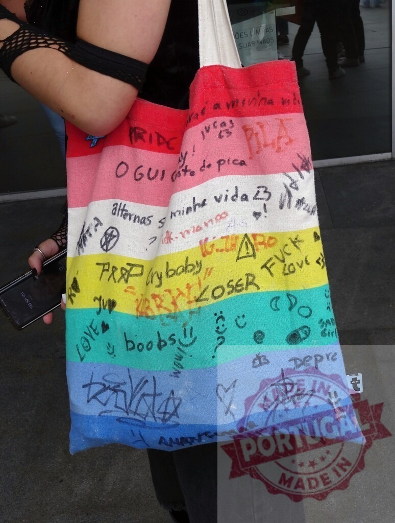 Person holding rainbow tote bag full of graffiti and doodles | Person carrying a colorful customized fabric bag with handwritten messages and symbols - Realized with Pictrs.com