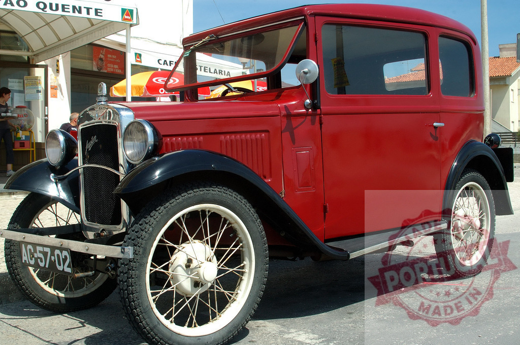 Restored Austin Seven Ruby red and black two-door saloon parked near a cafe | Classic red and black Austin Seven Ruby parked on the street in front of a cafe - Realized with Pictrs.com