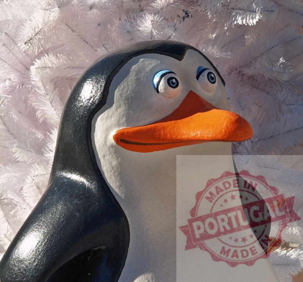 Decorative penguin statue posing in front of white christmas tree | Glossy penguin statue with big blue eyes and orange beak standing in front of a white christmas tree - Realisiert mit Pictrs.com