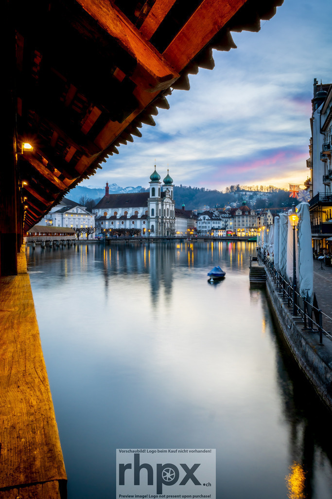 Blick durch die Kapellbrücke auf die Jesuitenkirche Luzern | Bogen. Fluss. Kontrast.Ein kreatives Spiel mit der Perspektive: Das moderne Element im Vordergrund lenkt den Blick kunstvoll auf die barocke Pracht der Jesuitenkirche. Ein spannender Dialog zwischen Form und Geschichte am Ufer der Reuss.Wähle unter "Produktauswahl" dein Wunschformat: Vom klassischen Wandbild über Puzzle &amp; Tassen bis zum digitalen Download (z.B. als Handy-Hintergrund). - Realisiert mit Pictrs.com