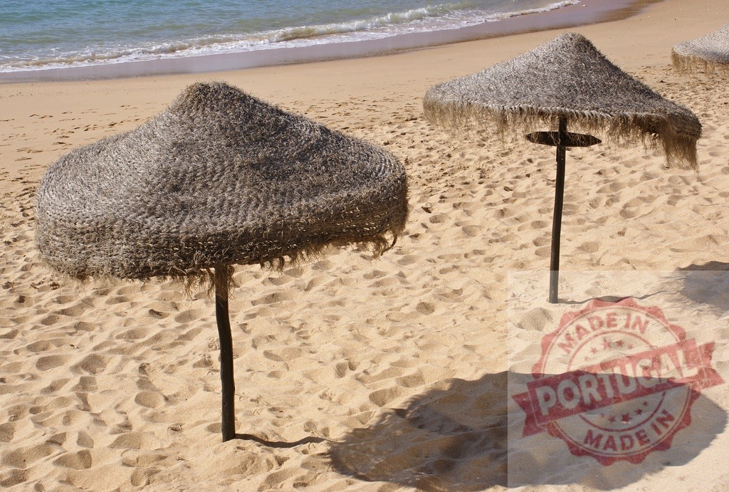 Straw umbrellas creating shade on sunny beach sand | Two straw umbrellas casting shadows on a warm sandy beach beside the ocean - Realisiert mit Pictrs.com