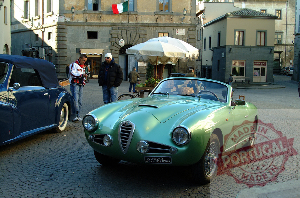 Vintage Alfa Romeo convertible parked in Italian town square | Classic mint green Alfa Romeo sports car stands in historic Italian piazza with cobblestones and flag - Realisiert mit Pictrs.com