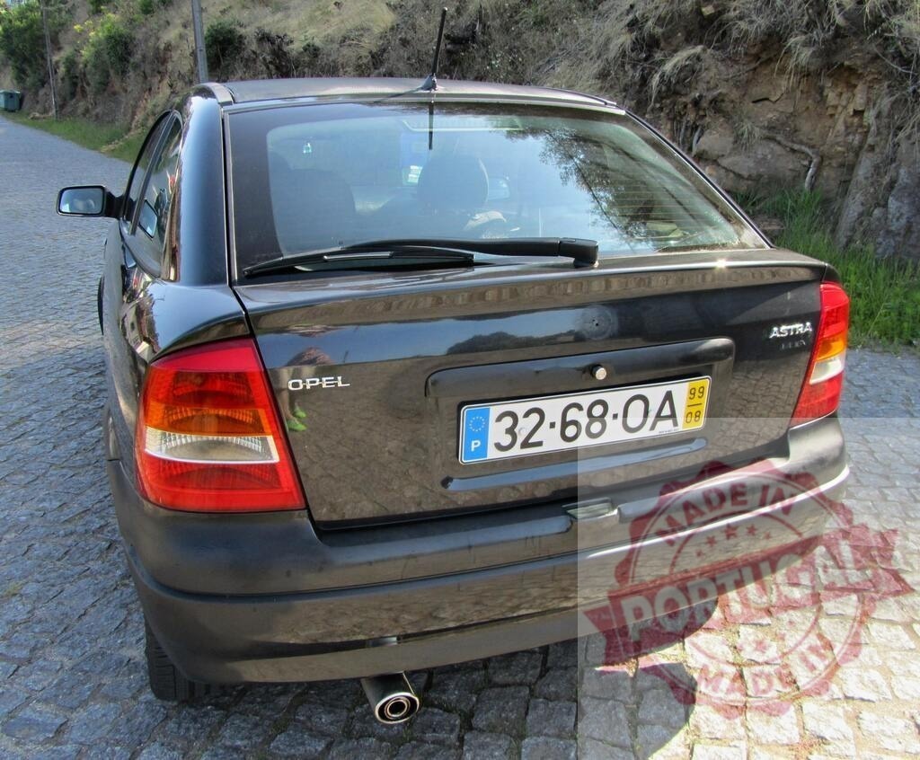 Opel Astra G parked on cobblestone road with vegetation in the background | Dark gray Opel Astra G car parked on a cobblestone road with vegetation in the background, showcasing its rear design - Realized with Pictrs.com