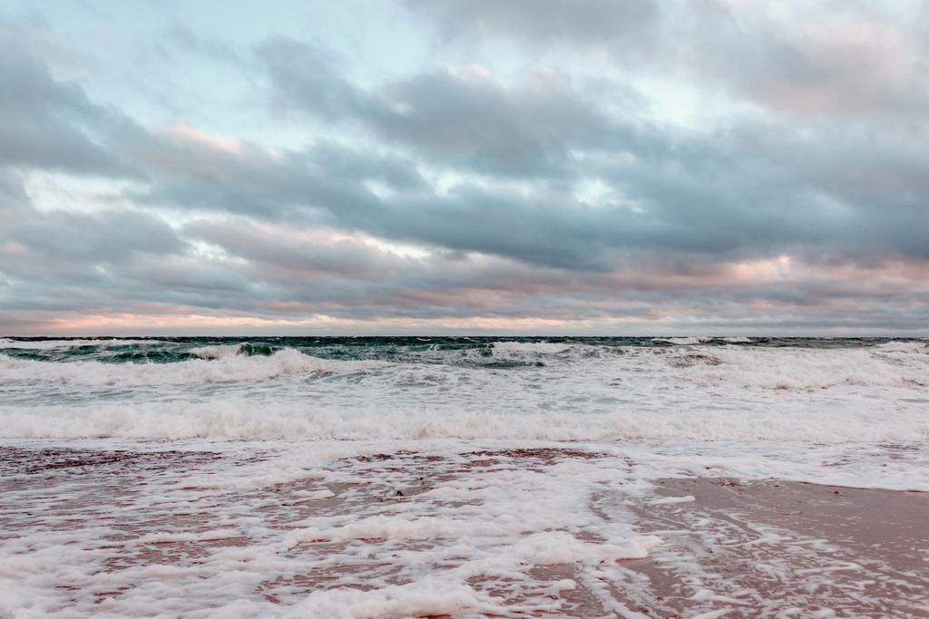 Wandbild: Wellen und Wolken im Morgenrot | Dieses Wandbild im Querformat zeigt Wellen und Gischt am Strand in überwiegend hellen Farben. Sowohl am Strand als auch im Meer ist viel weißer Schaum von der Gischt. Dadurch hat das Wandbild viele helle Bestandteile. Am Strand scheint das warme Beige des Sandstrands zwischen der Gischt durch. Der Himmel auf diesem Bild ist auch sehr malerisch. Am hellblauen Himmel sind graue Wolken, die Teilweise vom roten Licht der aufgehenden Sonne angeleuchtet werden. Holen Sie sich diese schöne maritime Morgenstimmung auf Leinwand, Aluminium-Platte oder als Glasbild. Ideal fürs Wohnzimmer, Schlafzimmer, Küche, den Arbeitsplatz oder die Ferienwohnung. Die Wandbilder werden individuell für Sie in vielen Abmessungen produziert. Daher passen die Ostseekult Wandbilder immer perfekt an Ihre Wände. - Realisiert mit Pictrs.com