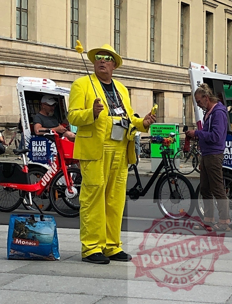 Yellow suited man entertaining tourists on Berlin street | Man in yellow suit standing on street, holding props, performing for tourists - Realized with Pictrs.com