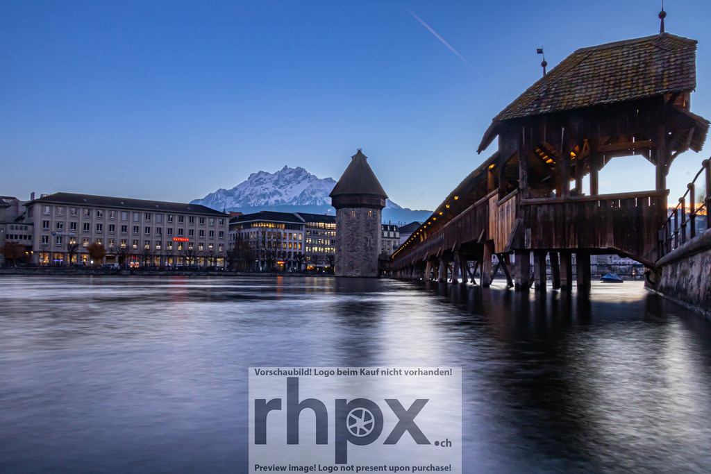 Kapellbrücke Luzern mit Pilatus im Hintergrund | Geschichte. Licht. Mythos. Das warme Leuchten der historischen Holzbrücke spiegelt sich sanft im Wasser der Reuss, während der schneebedeckte Pilatus im Hintergrund thront. Diese Langzeitbelichtung fängt die magische Atmosphäre und die Ruhe der Blauen Stunde in Luzern perfekt ein. Wähle unter "Produktauswahl" dein Wunschformat: Vom klassischen Wandbild über Puzzle &amp; Tassen bis zum digitalen Download (z.B. als Handy-Hintergrund). - Realisiert mit Pictrs.com