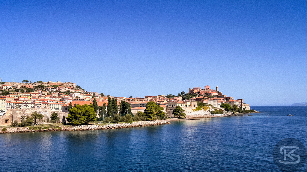 Panorama von Portoferraio: Historische Hafenstadt auf Elba – Exklusives Wandbild | Weitwinkelaufnahme der Hafenstadt Portoferraio auf Elba mit Blick über das blaue Meer auf die historischen Festungsmauern und die terrassenförmige Altstadt unter strahlend blauem Himmel. - Realisiert mit Pictrs.com