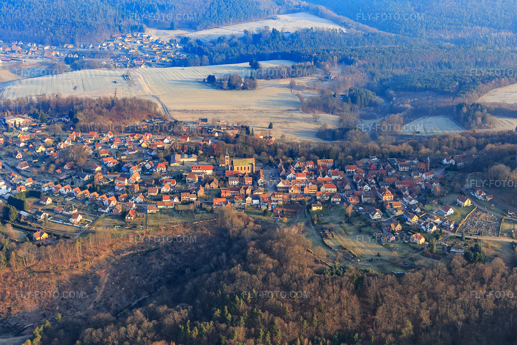 Aerial view: Village overview with Notre-Dame-Marie-Auxilliatrice church in Lichtenberg in the state Bas-Rhin, France. – Photo: IMG_105280.jpg taken on 03/25/2018 by Werner Riehm/FLY-FOTO.com – Resolution of the original: 5111 x 3408 px
