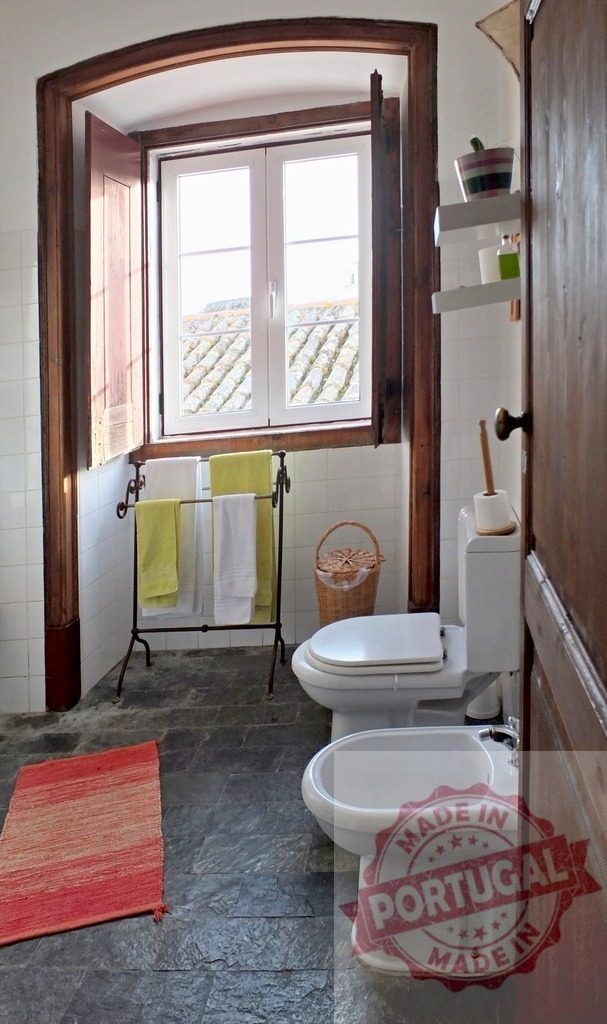 Rustic bathroom interior with toilet bidet and stone floor | Rustic bathroom interior featuring white tiles, a stone floor, and a window with wooden shutters - Realized with Pictrs.com