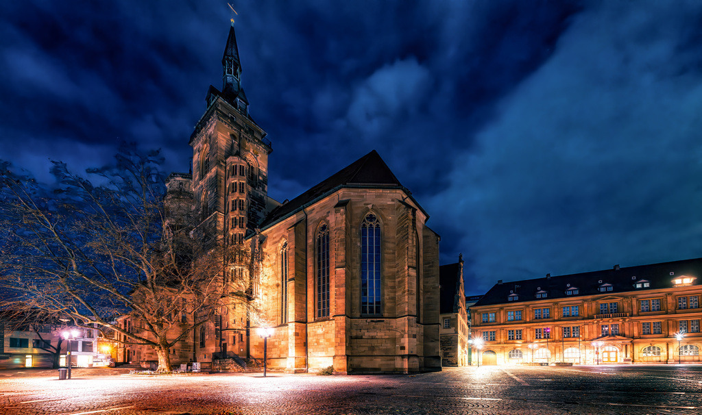 Die Stiftskirche in Stuttgart im fahlen Schein der Nacht | Das Bild zeigt die Stiftskirche Stuttgart bei Nacht. Sie ist der älteste und größte Kirchenbau in Stuttgart. Die Kirche wurde im Zweiten Weltkrieg zerstört und danach wieder aufgebaut. Ein markantes Merkmal ist der ungleiche Westturm, der eine Höhe von 61 Metern erreicht. In der Kirche befindet sich die Gruft der württembergischen Herzöge.  - Realisiert mit Pictrs.com