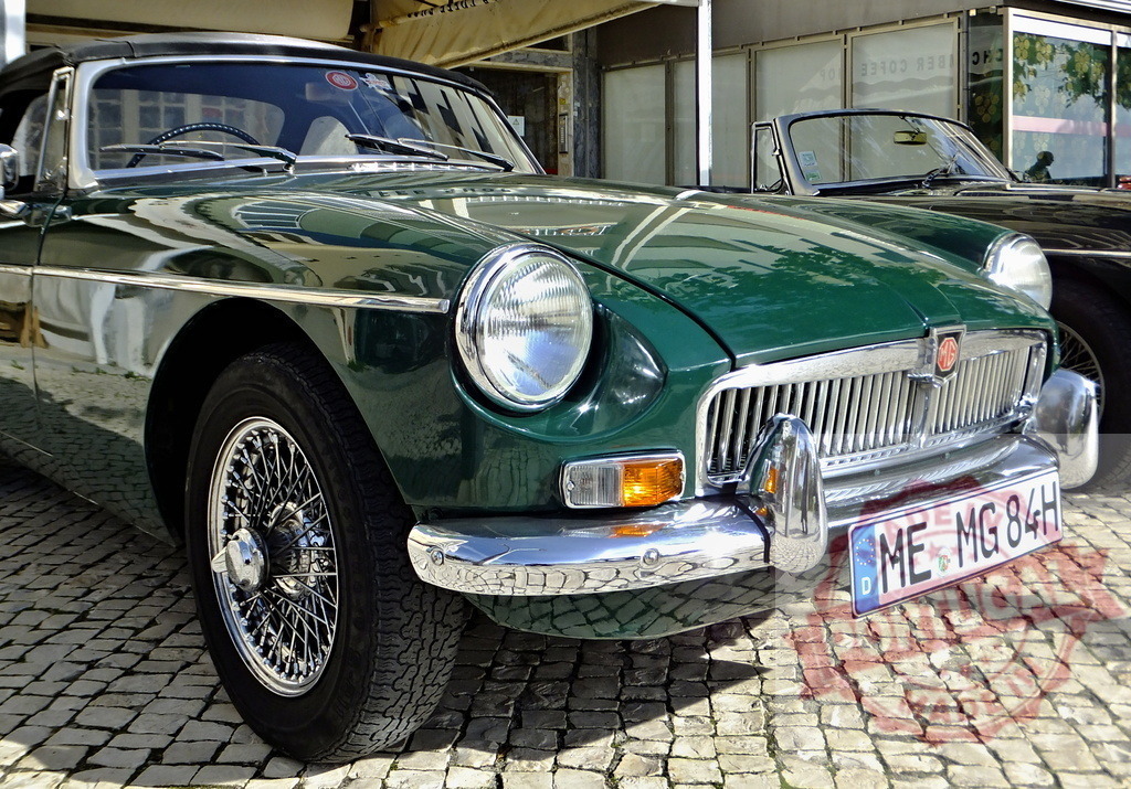 Shiny green MG parked on cobblestone street showcasing classic British design | Classic MG sports car parked on a cobblestone street, reflecting surrounding buildings in its polished paint - Realized with Pictrs.com