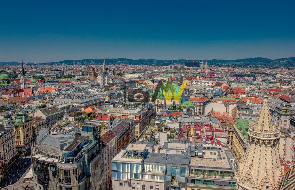 Panoramablick über die Stadt von Wien von oben----III | Die Aufnahme zeigt eine Luftaufnahme des ersten Bezirks von Wien, Österreich, aufgenommen vom Südturm des Stephansdoms aus. Der Stephansdom, auch bekannt als "Steffl", ist das Wahrzeichen Wiens und Sitz der Erzdiözese Wien. Die auf dem Bild sichtbare Turmspitze rechts gehört zum Südturm, der mit 136 Metern der höchste der vier Türme des Doms ist. Das Dach des Doms ist mit bunten Ziegeln gedeckt, die unter anderem den k.u.k. Doppeladler sowie die Wappen von Wien und Österreich zeigen.  - Realisiert mit Pictrs.com