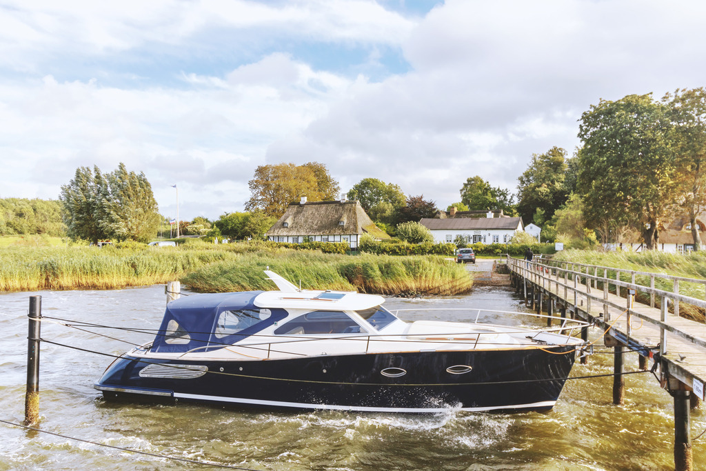 Akustikbild: Boot am Schleianleger in Sieseby an der Schlei | Dieses Akustikbild im Querformat zeigt ein Boot am Schleianleger in Sieseby zum Herbstbeginn. Auf der Schlei befinden sich kleine Wellen, die am Boot brechen. Auf der rechten Seite kann man einen Teile des Schleianlegers sehen. Am Ufer stehen zwei malerische Häuser. Der Himmel ist überwiegend bewölkt.