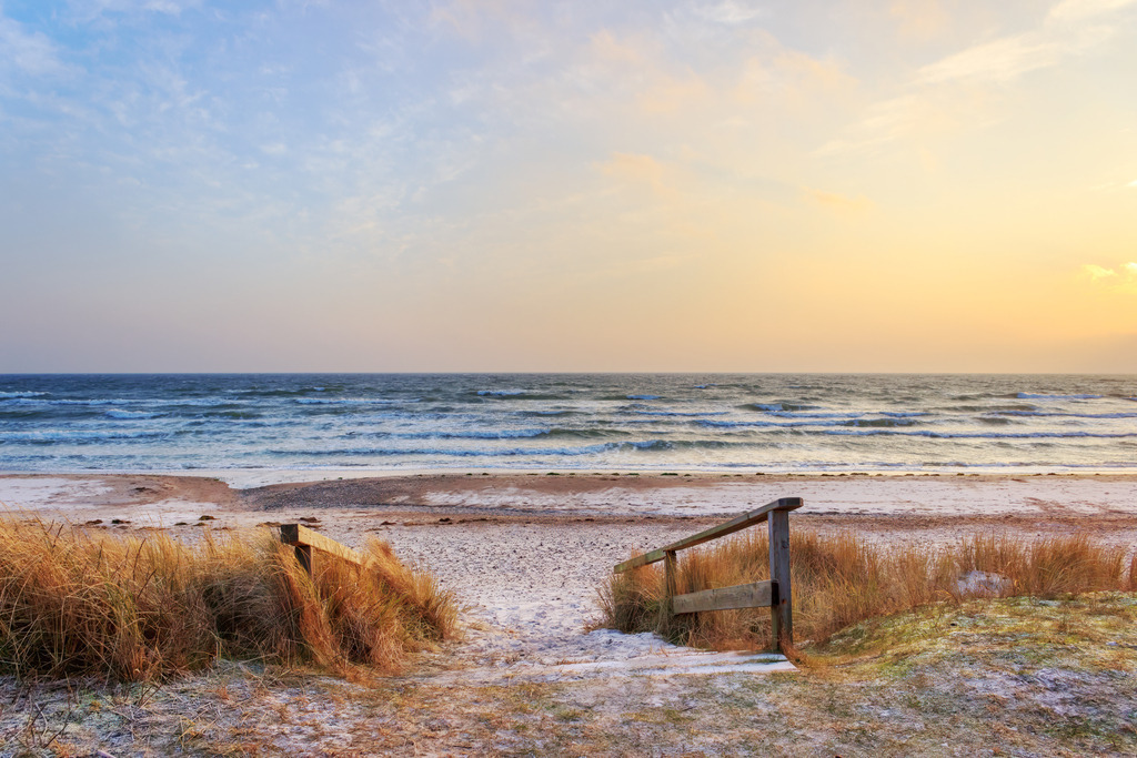 Wandbild: Morgendliche Lichtstimmung in Damp | Dieses Wandbild im Querformat zeigt einen sandigen Weg zum Strand in Damp, eingefasst von einem hölzernen Geländer und umgeben von hohem Gras. Die Szene ist in sanftes Morgenlicht getaucht – der Himmel leuchtet in warmen Orangetönen, während das Meer ruhig in der Ferne liegt. Die Komposition vermittelt Klarheit, Ruhe und die besondere Stimmung eines Tagesbeginns am Meer. Ideal für Wohnräume, Ferienunterkünfte oder Praxisräume mit maritimer Atmosphäre. Erhältlich als Leinwand, Acrylglas, Alu-Dibond, hochwertiger FineArt-Druck oder als schallabsorbierendes Akustikbild. - Realized with Pictrs.com