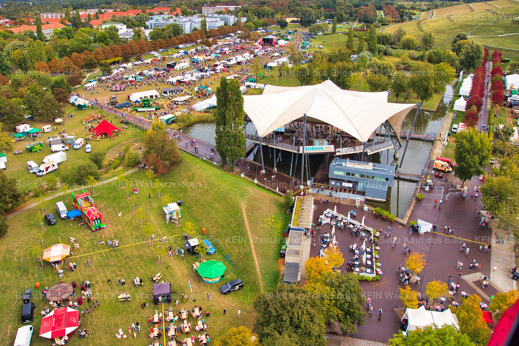 erntedankfest_magdeburg_9675 | Diese Luftaufnahme aus geringer Höhe zeigt das Erntedankfest im Elbauenpark aus einer beeindruckenden Perspektive. Rund um die Seebühne sind die zahlreichen Ausstellerstände, Aktionsflächen und Besucherbereiche hervorragend zu erkennen. Die niedrige Flughöhe des Tragschraubers vermittelt einen lebendigen Eindruck von der Größe und Vielfalt der Veranstaltung und macht die durchdachte Anordnung der einzelnen Bereiche besonders deutlich.Die Aufnahme entstand im Auftrag der Agrarmarketinggesellschaft Sachsen-Anhalt zur Dokumentation des Erntedankfestes. Luftbilder bieten Veranstaltern einen einzigartigen Überblick über das Gelände und zeigen eindrucksvoll, wie sich Aussteller, Präsentationsflächen und Besucherströme harmonisch in den Elbauenpark einfügen. Aus dieser Perspektive wird sichtbar, wie sorgfältig das Fest organisiert ist und welch attraktive Kulisse die Seebühne für eine solche Großveranstaltung bietet.Das Erntedankfest gehört zu den traditionsreichsten Veranstaltungen im Elbauenpark und verbindet regionale Landwirtschaft, kulinarische Spezialitäten, Handwerk und Unterhaltung für die ganze Familie. Diese Luftaufnahme hält nicht nur die besondere Atmosphäre des Festes fest, sondern dokumentiert zugleich einen wichtigen Treffpunkt für Besucher aus ganz Sachsen-Anhalt. - Realisiert mit Pictrs.com