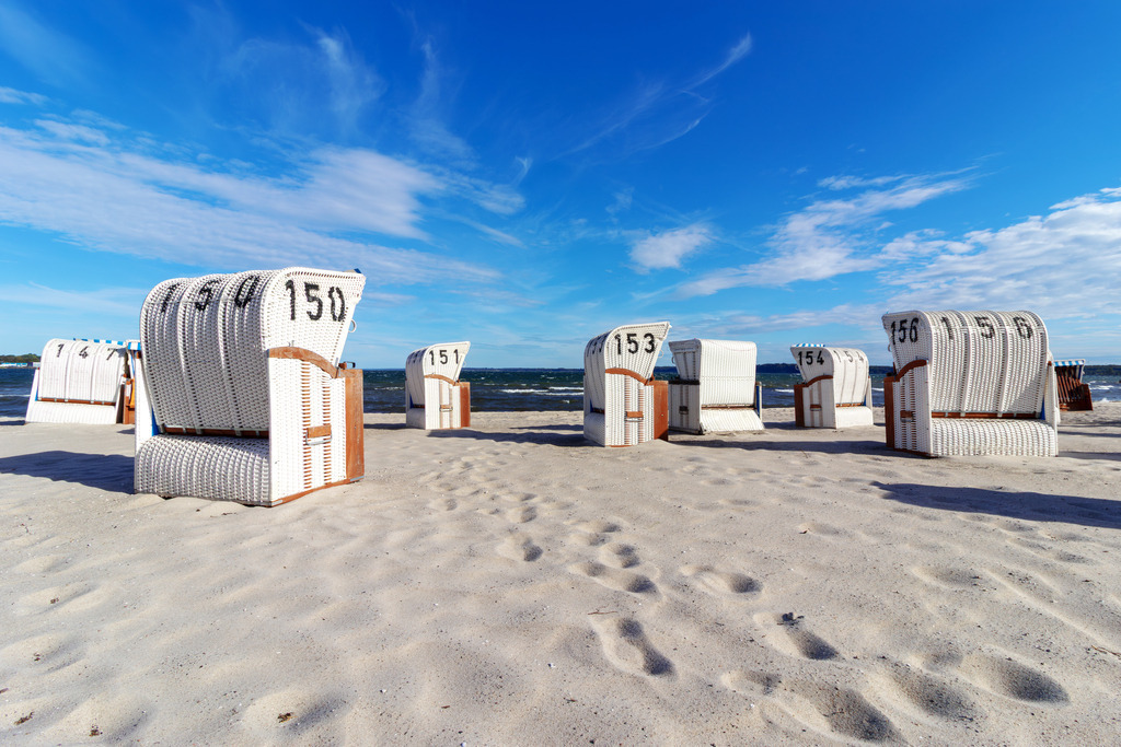 Wandbild: Sand, Himmel, Meer – Küstenruhe in Eckernförde | Dieses Wandbild zeigt den Sandstrand von Eckernförde an der Ostsee. Weiße Strandkörbe stehen in geordneter Reihe auf dem hellen Sand, ihre Nummern gut sichtbar – ein vertrautes Bild norddeutscher Strandkultur. Der Himmel ist weit und blau, mit leichten Wolken, das Meer ruhig und leicht bewegt. Die Szene wirkt klar und einladend, als würde der Tag gerade beginnen. Die Komposition lebt vom Zusammenspiel aus Struktur, Licht und Weite. Ideal als Wandbild für maritime Wohnkonzepte – ob als Leinwandbild, Acrylglasbild, Alu-Dibond FineArt Print oder als Akustikbild. Ein frischer Akzent für Wohnzimmer, Büro oder Ferienwohnung. - Realisiert mit Pictrs.com