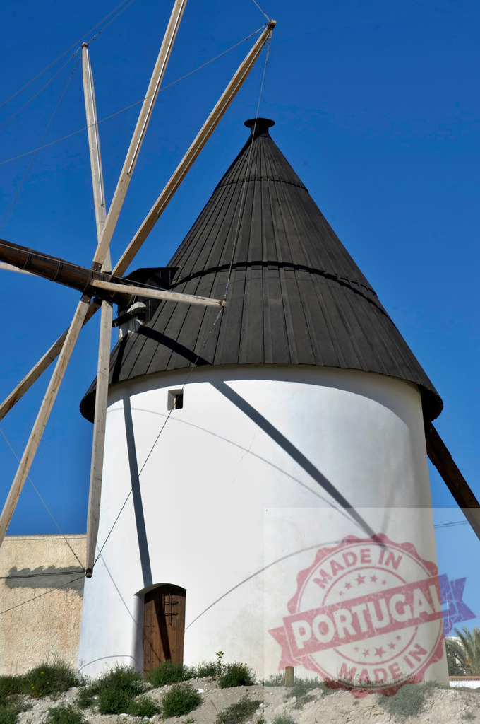 Traditional Spanish windmill against a clear blue sky | White stone windmill with a black conical roof and wooden sails on a sunny day - Realisiert mit Pictrs.com