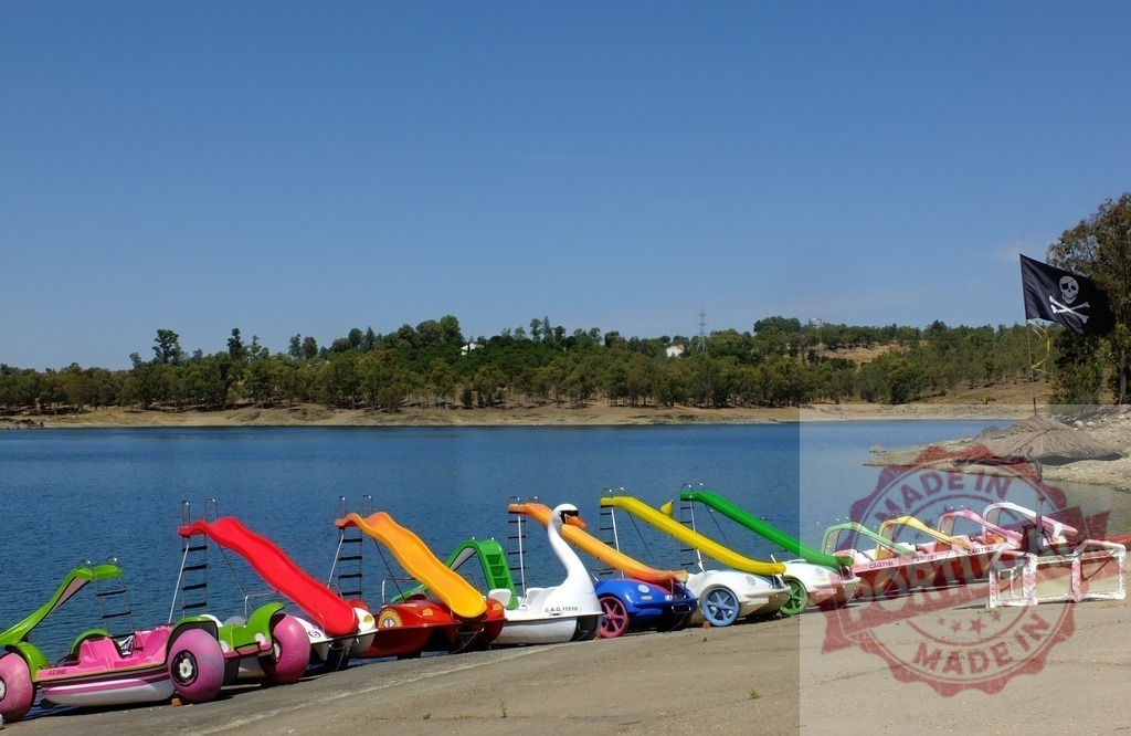 Colorful pedal boats on lake shore awaiting summer fun. Spain - Extremadura | Row of various pedal boats with slides on a lake shore on a clear summer day - Realisiert mit Pictrs.com