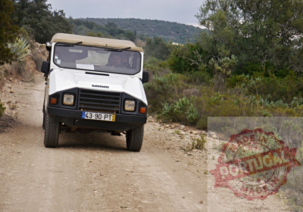 White off-road vehicle driving on dirt track in Portugal | Off-road vehicle driving on a dusty rural track through nature with hills in the background - Realized with Pictrs.com