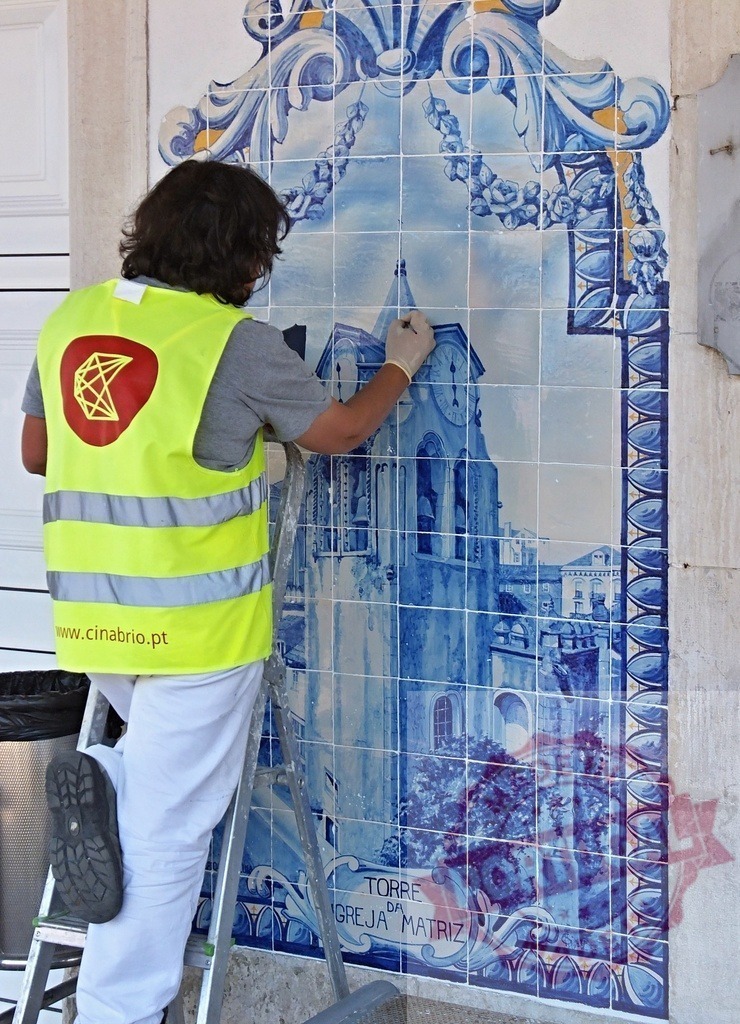 Worker restoring azulejo tile mural in Portugal | Skilled worker carefully restoring a traditional blue Portuguese azulejo tile mural on a building facade - Realized with Pictrs.com