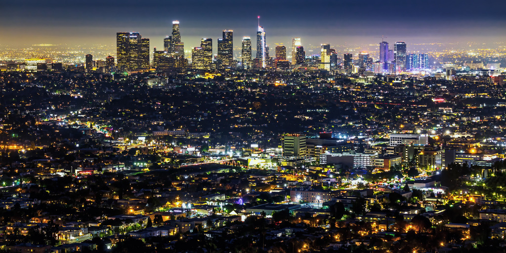Wandbild - Leuchtende Nächte in Los Angeles | Dieses eindrucksvolle Bild zeigt die Skyline von Los Angeles bei Nacht, die in einem Meer aus funkelnden Lichtern erstrahlt. Die Wolkenkratzer und hohen Gebäude leuchten hell und dominieren den Horizont, während sich das Stadtbild weit in die Ferne erstreckt. Die vielen Lichter der Straßen, Gebäude und Häuser schaffen ein lebendiges und dynamisches Ambiente. Der Kontrast zwischen den dunklen Silhouetten der Gebäude und den hellen Lichtern fängt die Energie und das pulsierende Leben der Stadt ein. Die klare Nacht und der leicht dunstige Himmel verstärken die Tiefe und Weite der Szene.