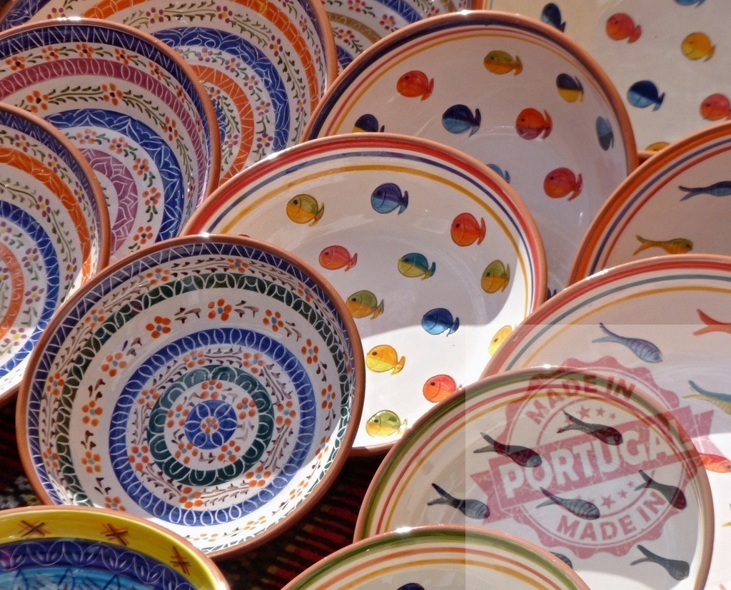 Assortment of vibrant handmade pottery bowls and dishware on display | Colorful hand-painted ceramic plates displaying fish and floral patterns - Realisiert mit Pictrs.com