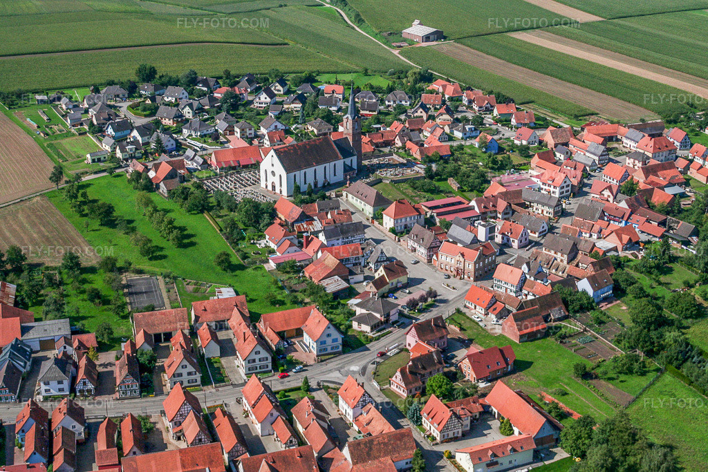 Aerial view: Village center with Église Saint-Barthélemy de Schleithal from the northeast in Schleithal in the state Bas-Rhin, France. – Photo: IMG_3565.jpg taken on 08/31/2006 by Werner Riehm/FLY-FOTO.com – Resolution of the original: 3021 x 2014 px
