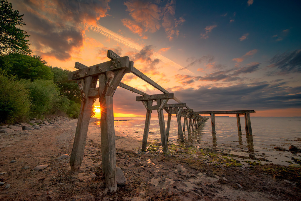 Alte Seebrücke von Quern an der Flensburger Förde | Auf dem Foto sind die Überreste der Beeindruckenden alte Seebrücke von Quern an der Flensburger Förde zu sehen. Die robusten Holzpfähle zeigen Spuren vergangener Tage. Das Foto fängt die nostalgische Schönheit und den Charme der alten Seebrücke von Quern ein. Es erinnert an vergangene Zeiten, als die Seebrücke noch ein belebter Treffpunkt für Einheimische und Touristen war. Gleichzeitig strahlt es Ruhe und Gelassenheit aus und lädt den Betrachter ein, einen Moment der Stille und des Innehaltens zu genießen.