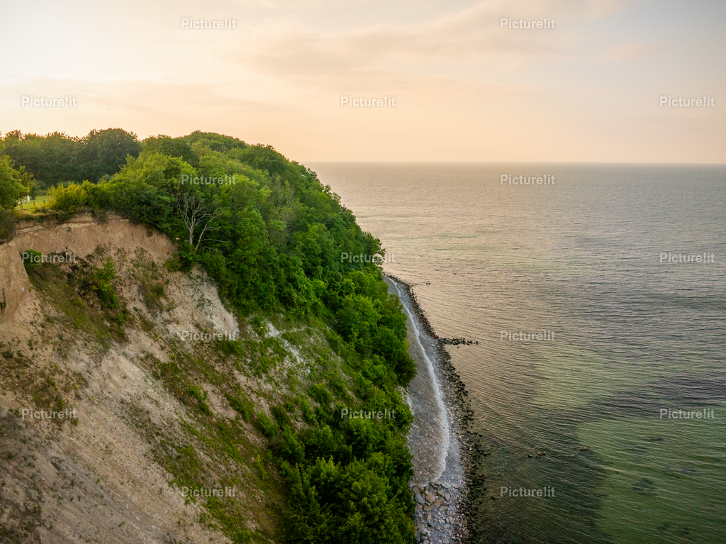 Ostsee Klippen  | Ein atemberaubender Blick über die steilen Klippen an der Ostsee. Die Felsen fallen markant zum Meer hinab und treffen auf das endlose Blau des Wassers, das im Sonnenlicht glitzert. Der Horizont wirkt weit und offen, während die Natur in ihrer ursprünglichen Schönheit und Ruhe erscheint. Die Mischung aus rauer Küstenlinie und sanftem Meer schafft eine einzigartige Stimmung zwischen Kraft und Harmonie – ein Moment, der den Zauber der Ostsee perfekt einfängt. - Realisiert mit Pictrs.com