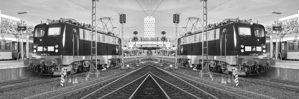 E-Lokomotive Baureihe 140 | Im Bahnhof Hamburg Altona steht eine E-Lok der Baureihe 140 an einem Bahnsteig. Das schwarz-weiße Bild wurde horizontal gespiegelt, wodurch die Szenerie eine sehr dynamische Ausprägung erhält. - Realisiert mit Pictrs.com