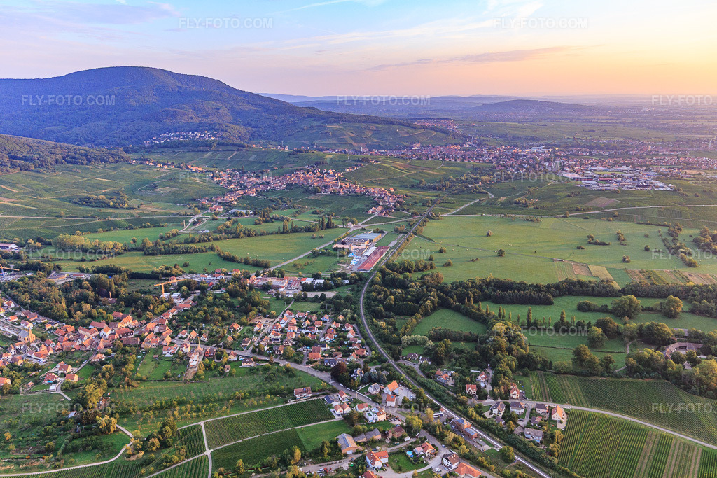 Aerial view: Evening view of the town along the railway line from the south in Eichhoffen in the state Bas-Rhin, France. – Photo: IMG_137949.jpg taken on 08/19/2023 by Werner Riehm/FLY-FOTO.com – Resolution of the original: 5472 x 3648 px
