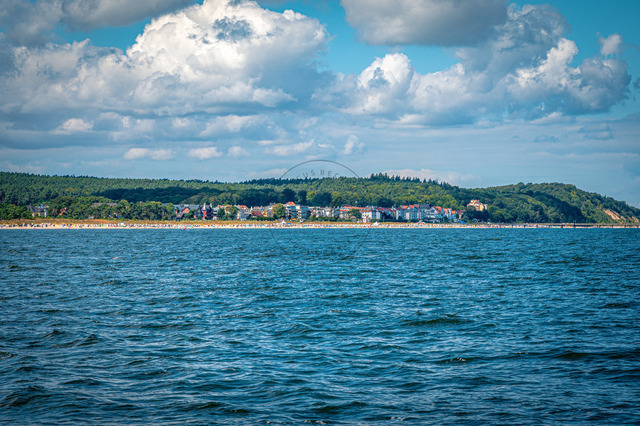 2026-08-08_12-42-12_850 | Blick auf bewaldete Küste mit Gebäuden am Wasser, unter einem bewölkten blauen Himmel, Bansin, Usedom, Mecklenburg-Vorpommern, Deutschland - Realisiert mit Pictrs.com