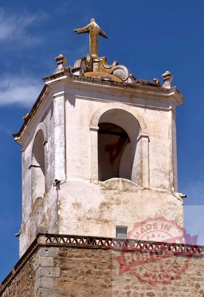 Christ statue on historic church bell tower against blue sky. Extremdura - Spain | Christian statue on church bell tower with arches and stone wall below a blue sky - Realized with Pictrs.com
