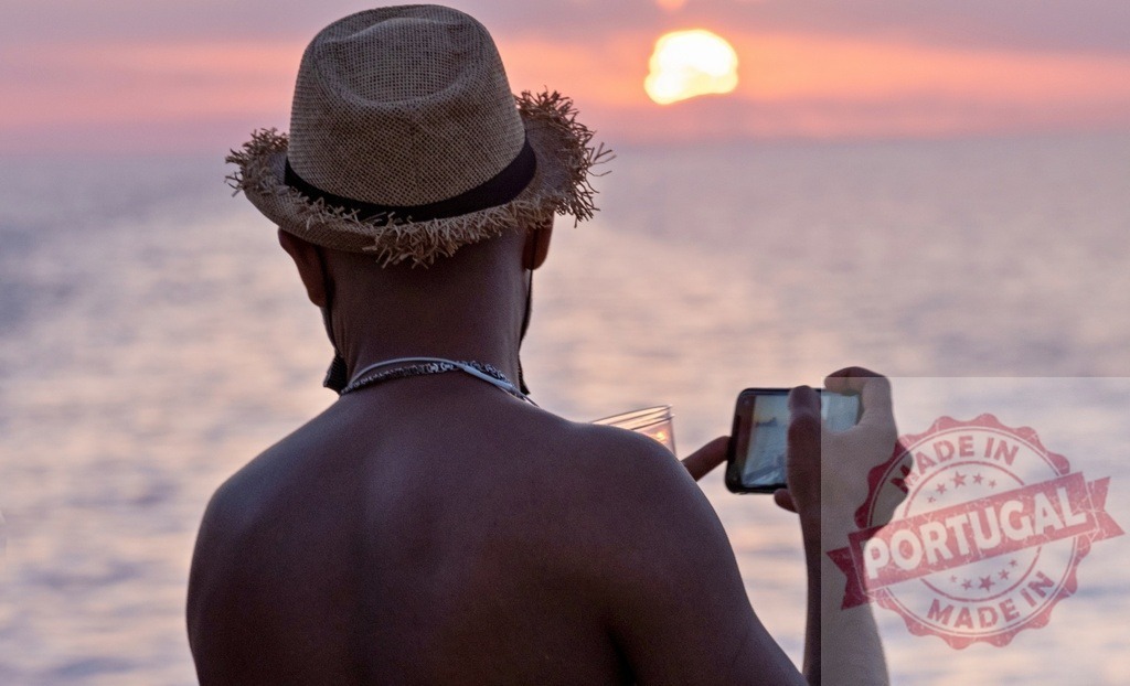 Man in hat filming sunset with smartphone | Man capturing sunset over ocean with smartphone on vacation - Realized with Pictrs.com