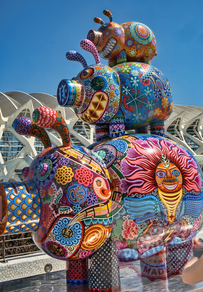 Colorful pig urban art sculpture in Valencia, Spain | Ornate pig sculptures stacked against modern architecture and a clear blue sky - Realized with Pictrs.com