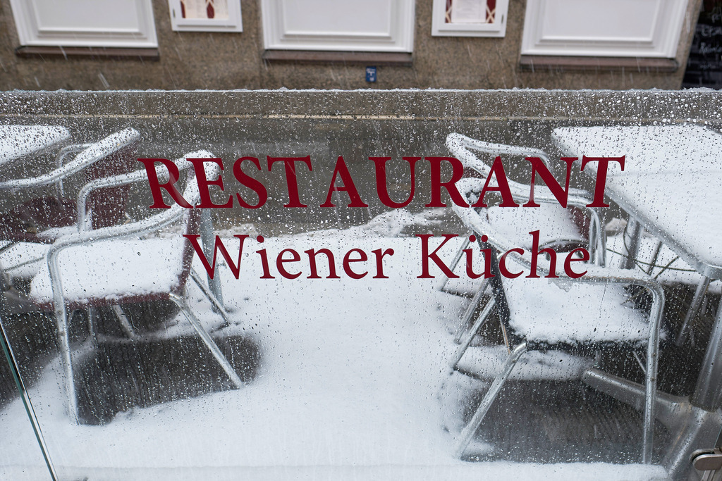 verschneite leere Tische und Stühle | Wien, Austria - December 09, 2021: verschneite leere Tische und Stühle mit Glaswand und Aufschrift Restaurant Wiener Küche. - Realisiert mit Pictrs.com